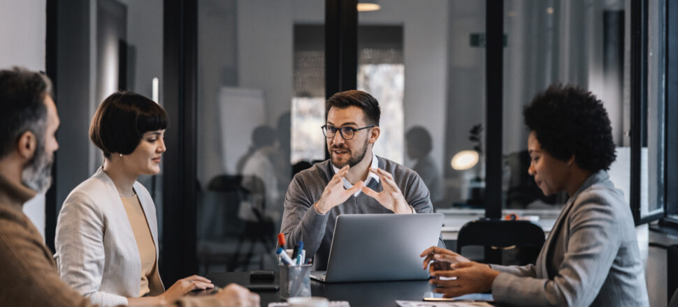 A focused businessman is sitting at the meeting room with colleagues and brainstorming about project.